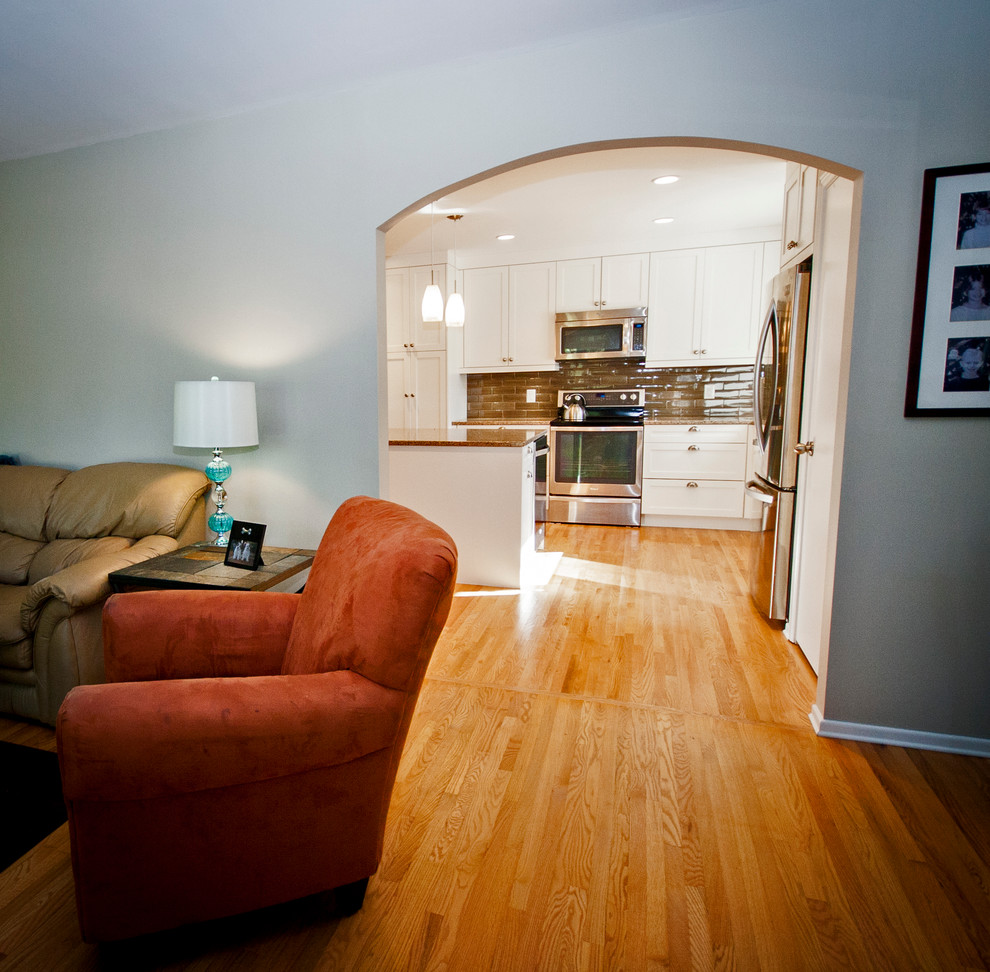 Mid-sized transitional l-shaped light wood floor eat-in kitchen photo with a double-bowl sink, white cabinets, quartz countertops, brown backsplash, ceramic backsplash, stainless steel appliances, an island and shaker cabinets