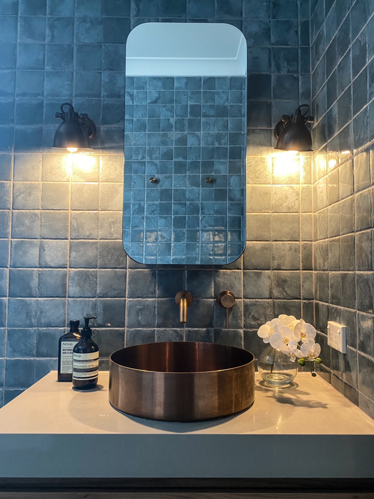 Foto på ett litet orientaliskt grå badrum, med släta luckor, bruna skåp, en vägghängd toalettstol, blå kakel, keramikplattor, blå väggar, klinkergolv i keramik, ett fristående handfat, bänkskiva i kvarts och grått golv