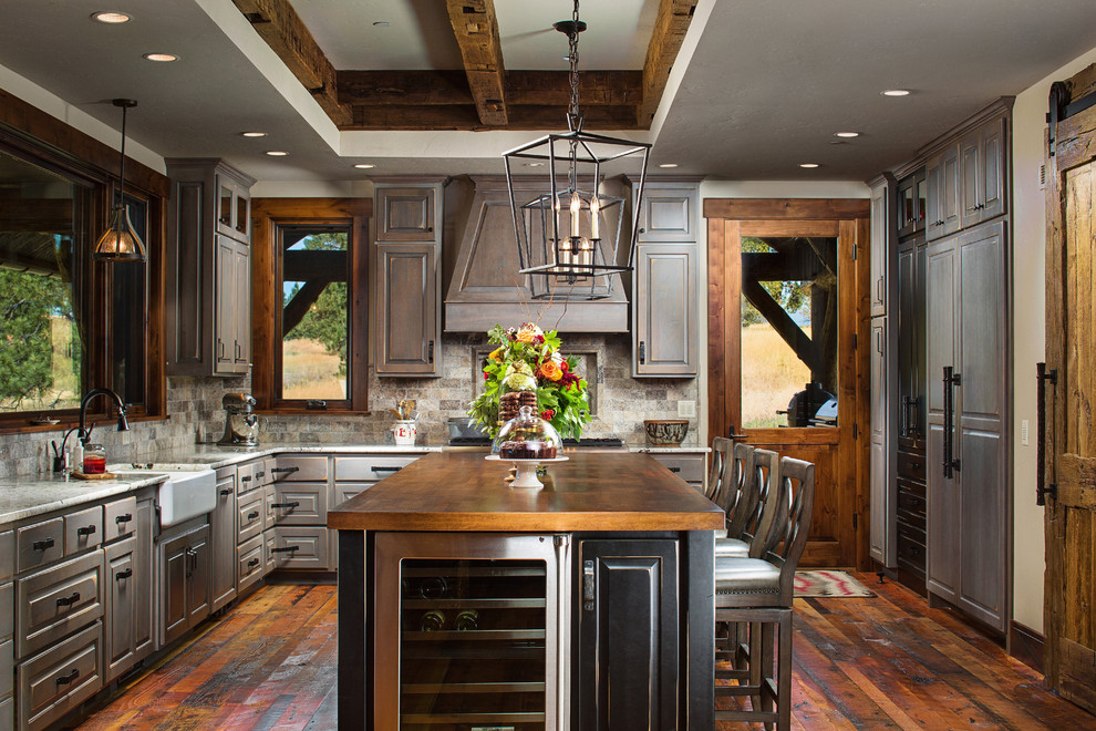 Example of a large mountain style l-shaped dark wood floor kitchen design with a farmhouse sink, raised-panel cabinets, distressed cabinets, brown backsplash, paneled appliances, an island and copper countertops