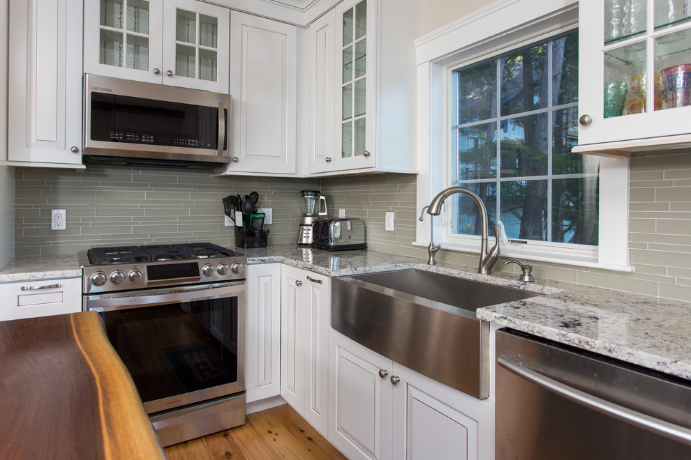 Mid-sized traditional separate kitchen in Boston with a farmhouse sink, glass-front cabinets, white cabinets, quartzite benchtops, beige splashback, glass tile splashback, stainless steel appliances, medium hardwood floors and with island.
