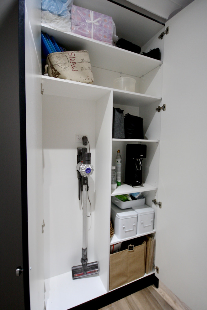 This is an example of a mid-sized transitional galley dedicated laundry room in Sydney with an undermount sink, shaker cabinets, black cabinets, quartz benchtops, white splashback, subway tile splashback, grey walls, light hardwood floors, a side-by-side washer and dryer, brown floor, white benchtop and recessed.