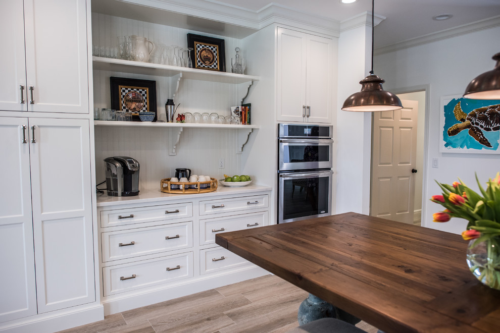 Photo of a mid-sized transitional l-shaped eat-in kitchen in Other with an undermount sink, shaker cabinets, white cabinets, solid surface benchtops, green splashback, glass tile splashback, stainless steel appliances, medium hardwood floors and with island.