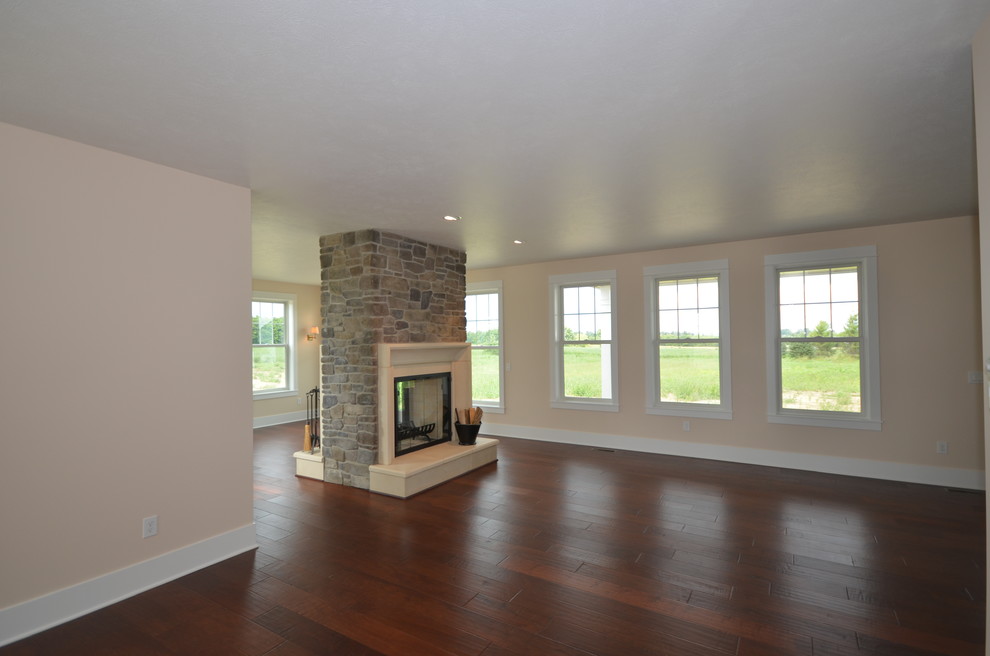 Large country open concept living room in Grand Rapids with yellow walls, dark hardwood floors, a two-sided fireplace, a stone fireplace surround and a wall-mounted tv.