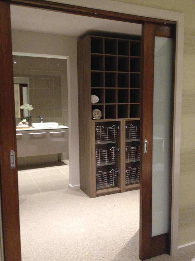 Photo of a large beach style gender-neutral dressing room in Melbourne with open cabinets, medium wood cabinets, carpet and beige floor.