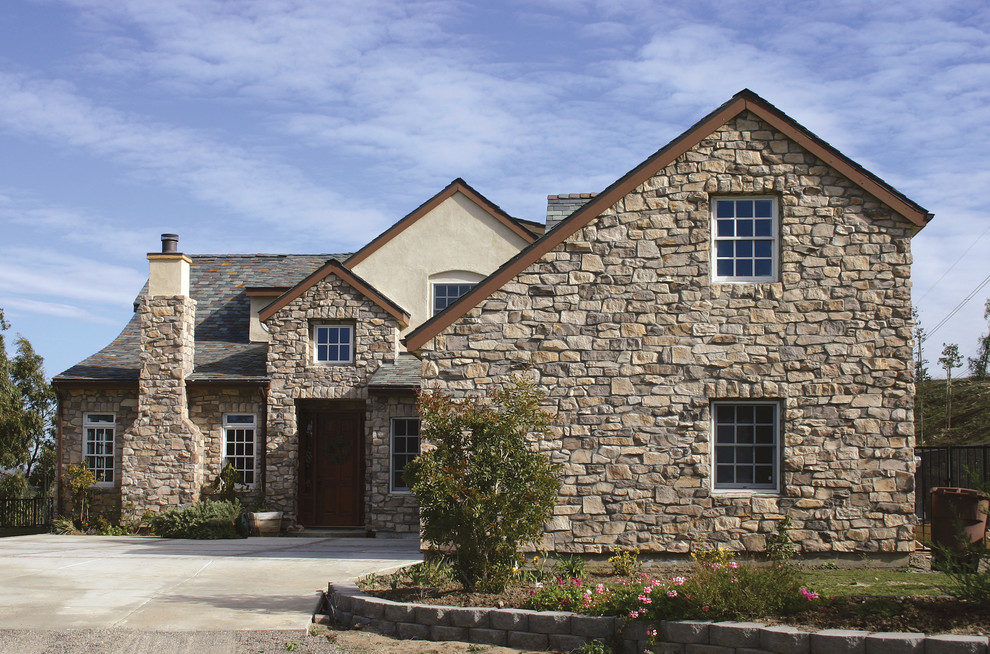 Inspiration for a large rustic beige two-story stone gable roof remodel