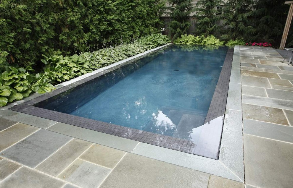 This is an example of a small modern backyard rectangular lap pool in Toronto with natural stone pavers.