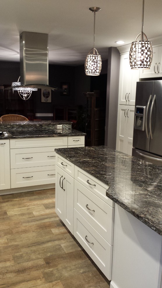 Inspiration for a mid-sized transitional l-shaped light wood floor eat-in kitchen remodel in New York with a double-bowl sink, shaker cabinets, white cabinets, granite countertops, gray backsplash, mosaic tile backsplash, stainless steel appliances and an island