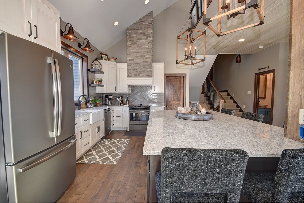 Mid-sized transitional u-shaped medium tone wood floor eat-in kitchen photo with a farmhouse sink, raised-panel cabinets, white cabinets, granite countertops, gray backsplash, stone tile backsplash, stainless steel appliances and an island
