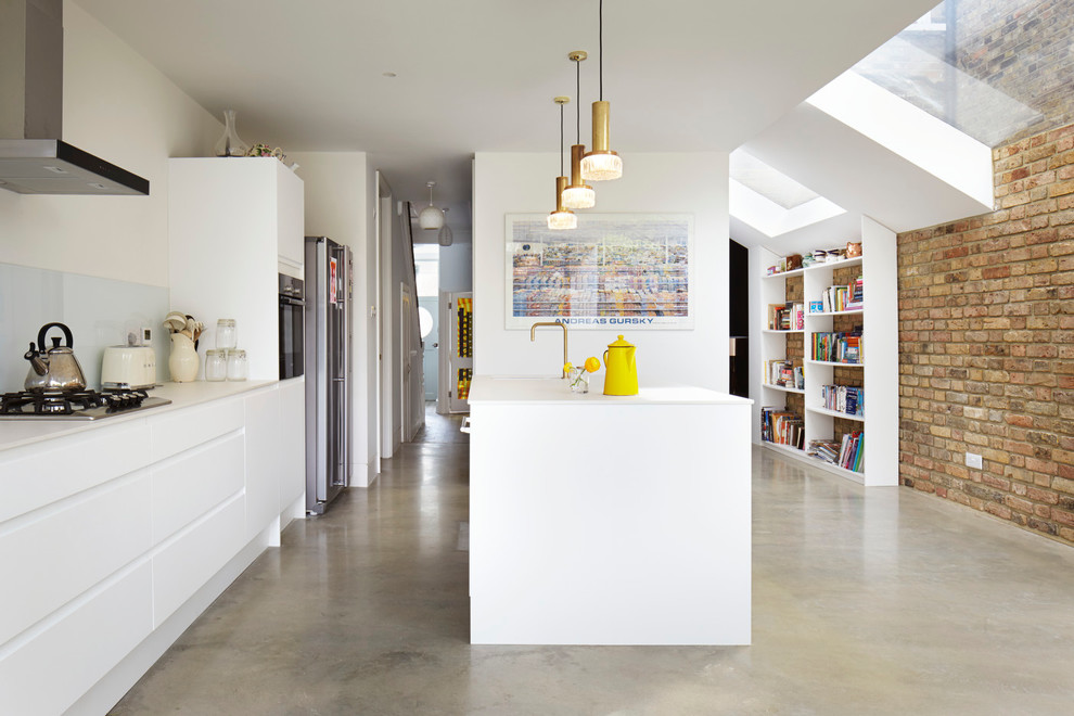 Small contemporary single-wall open plan kitchen in Other with a farmhouse sink, flat-panel cabinets, white cabinets, solid surface benchtops, white splashback, glass sheet splashback, white appliances, concrete floors and with island.