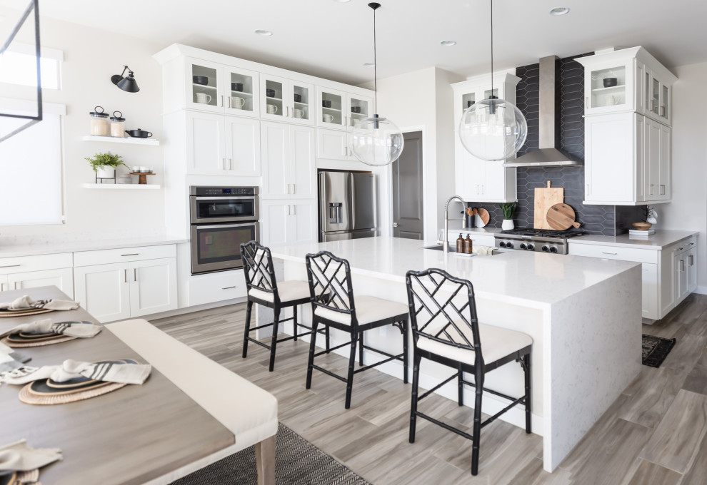 Inspiration for a large transitional l-shaped eat-in kitchen in Phoenix with shaker cabinets, white cabinets, quartz benchtops, with island, white benchtop, an undermount sink, black splashback, stainless steel appliances and grey floor.