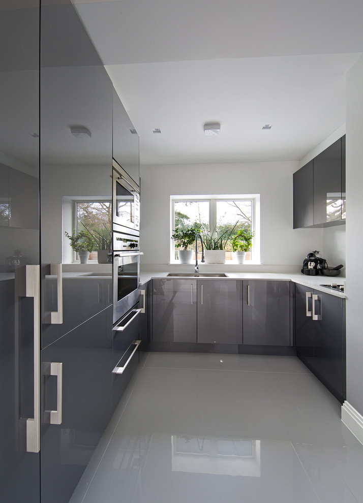 Design ideas for a mid-sized contemporary u-shaped kitchen pantry in Hertfordshire with an undermount sink, flat-panel cabinets, grey cabinets, solid surface benchtops, porcelain floors and with island.