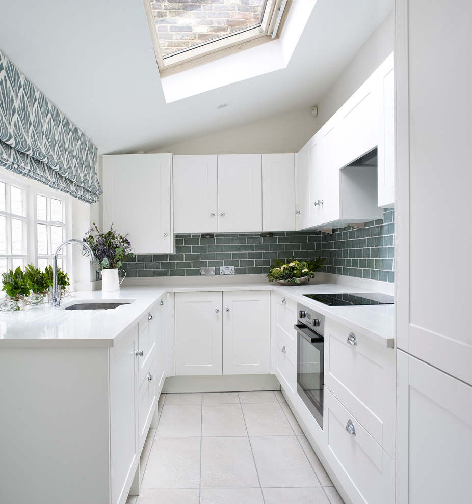 This is an example of a transitional u-shaped separate kitchen in London with an undermount sink, shaker cabinets, white cabinets, grey splashback, subway tile splashback and stainless steel appliances.