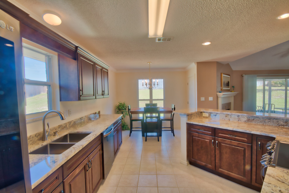 Photo of a mid-sized l-shaped eat-in kitchen in Other with an undermount sink, raised-panel cabinets, dark wood cabinets, granite benchtops, stainless steel appliances, cement tiles, a peninsula, pink floor and beige benchtop.