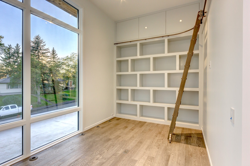 Photo of a mid-sized modern home office in Calgary with a library, white walls and light hardwood floors.