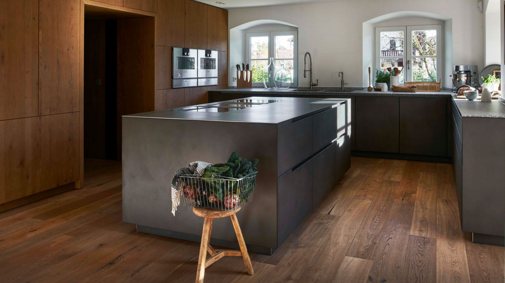 Offene Moderne Küche mit grauen Schränken, Edelstahl-Arbeitsplatte, gebeiztem Holzboden und Kücheninsel in München