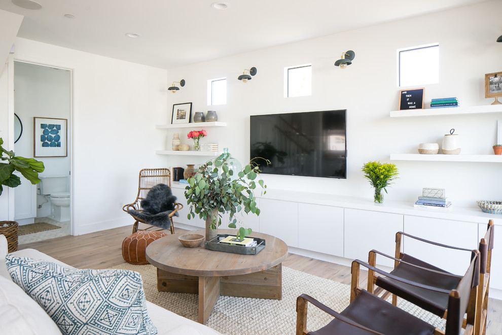 Photo of a beach style living room in Orange County with white walls, light hardwood floors, a wall-mounted tv and beige floor.