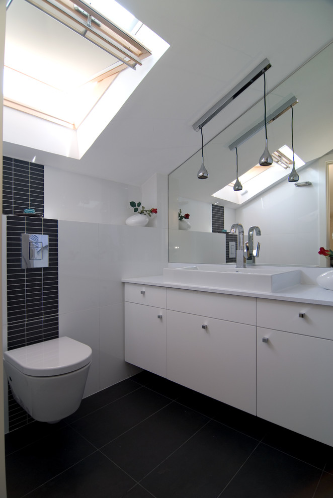 This is an example of a contemporary powder room in Tel Aviv with a vessel sink, flat-panel cabinets, white cabinets, a wall-mount toilet, black tile and black floor.