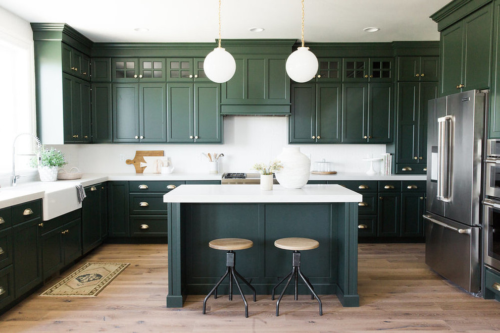 Large transitional kitchen in Salt Lake City with a farmhouse sink, green cabinets, white splashback, stainless steel appliances, with island, shaker cabinets and light hardwood floors.