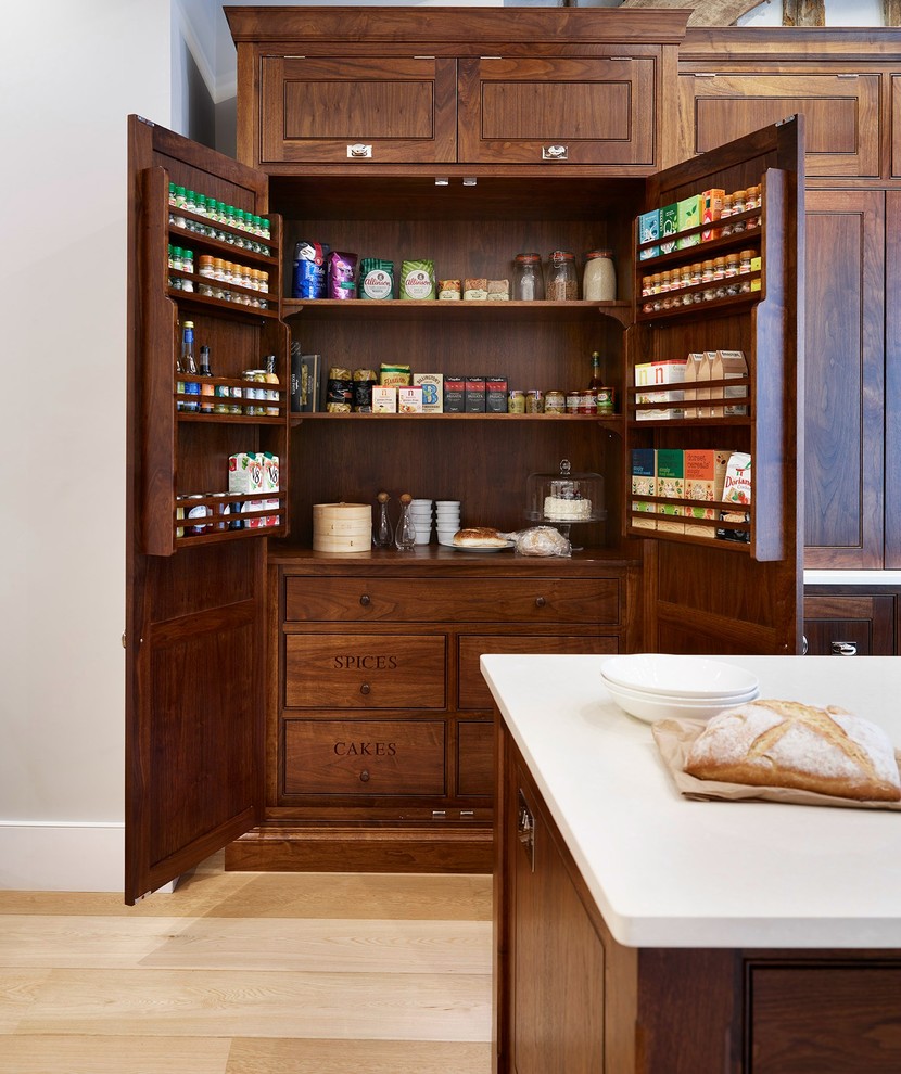 Inspiration for a large traditional galley kitchen pantry in Essex with shaker cabinets, dark wood cabinets, light hardwood floors, with island, solid surface benchtops and stainless steel appliances.