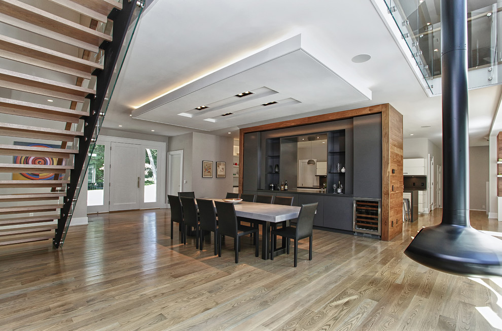 This is an example of a large contemporary open plan dining in New York with white walls, light hardwood floors, a hanging fireplace and a metal fireplace surround.