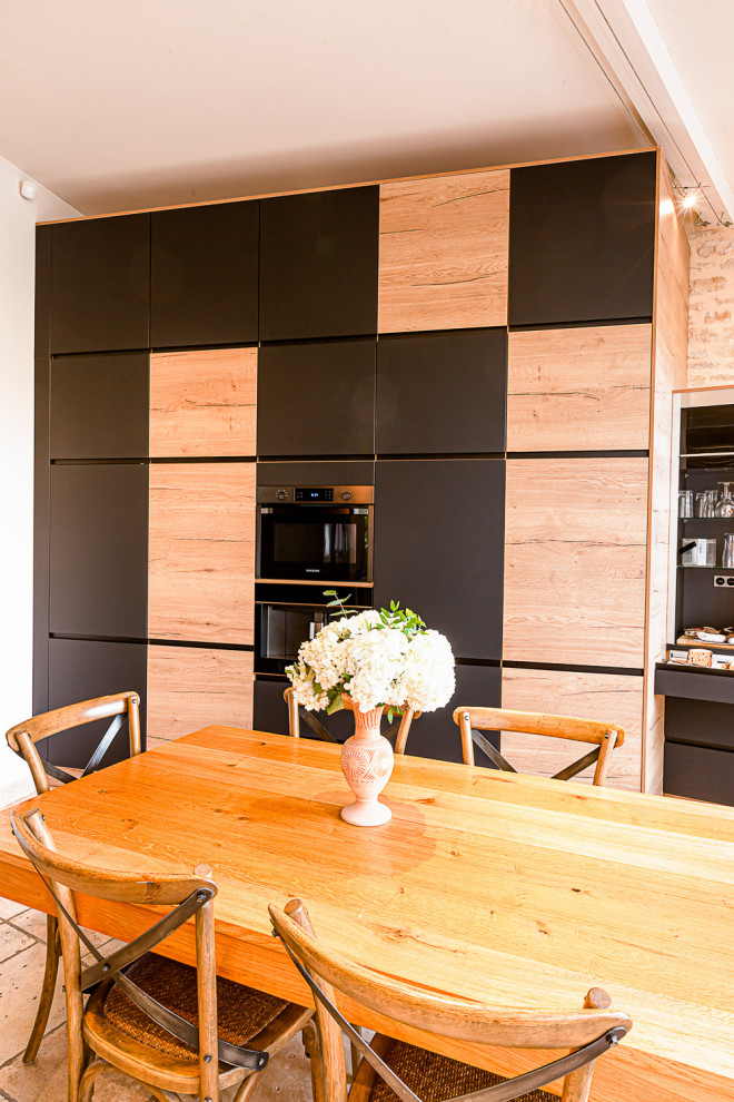 Ejemplo de cocina industrial extra grande abierta con puertas de armario negras, electrodomésticos negros y suelo beige