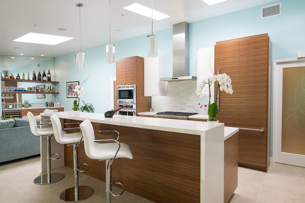 Mid-sized contemporary l-shaped open plan kitchen in Los Angeles with a drop-in sink, flat-panel cabinets, medium wood cabinets, solid surface benchtops, white splashback, stainless steel appliances, porcelain floors and with island.
