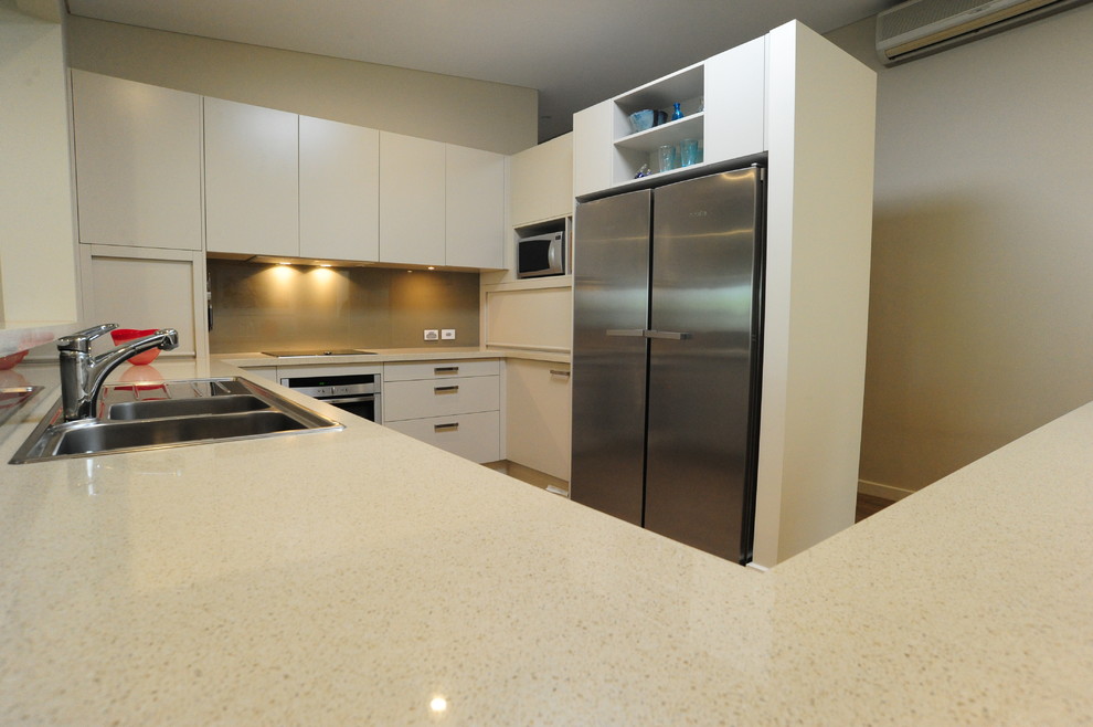 This is an example of a mid-sized u-shaped eat-in kitchen in Adelaide with white cabinets, solid surface benchtops, brown splashback, glass sheet splashback, stainless steel appliances and with island.