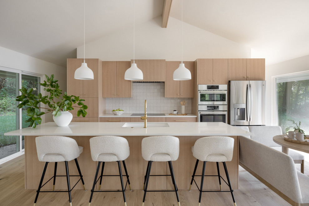 Mid-sized beach style single-wall medium tone wood floor, brown floor and vaulted ceiling eat-in kitchen photo in Seattle with an integrated sink, flat-panel cabinets, light wood cabinets, quartz countertops, white backsplash, ceramic backsplash, stainless steel appliances, an island and white countertops