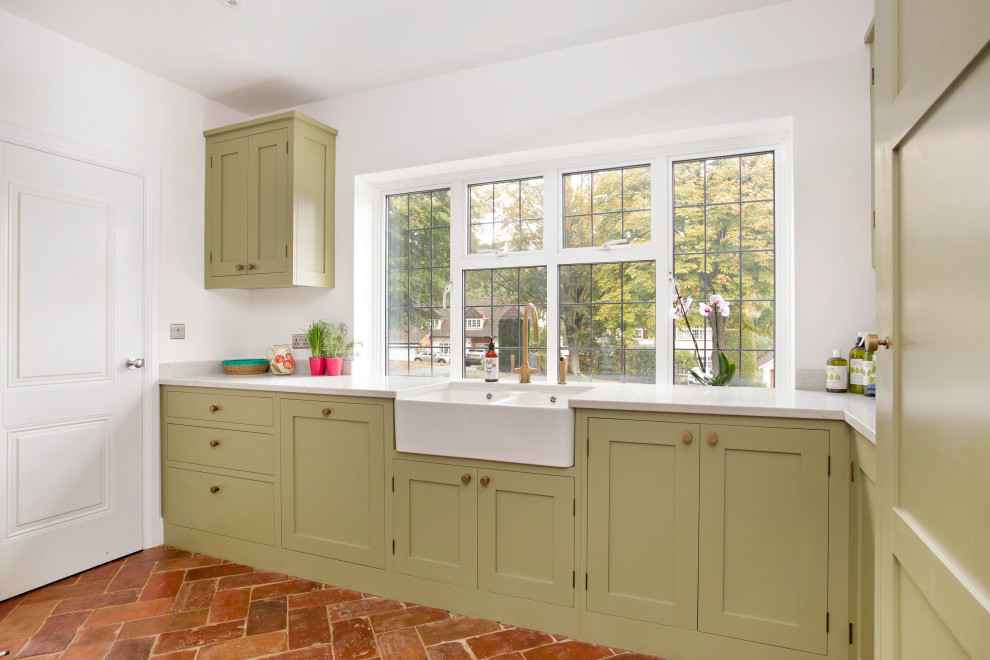 Inspiration for a medium sized classic l-shaped separated utility room in London with a belfast sink, shaker cabinets, green cabinets, quartz worktops, white walls, terracotta flooring, a concealed washer and dryer, orange floors and white worktops.
