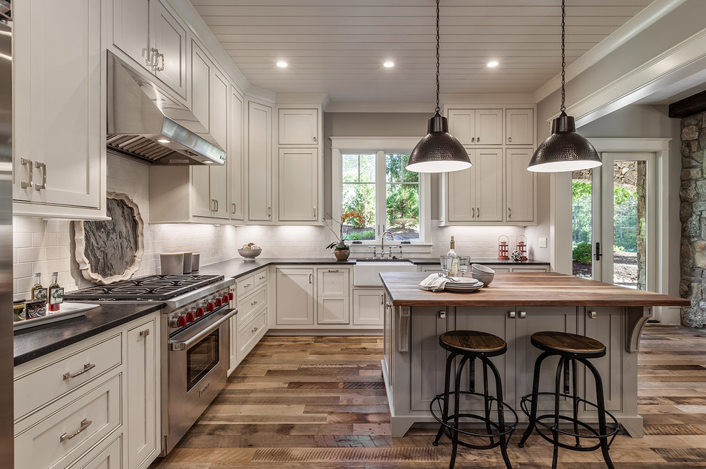 Inspiration for a mid-sized rustic l-shaped light wood floor open concept kitchen remodel with a farmhouse sink, recessed-panel cabinets, white cabinets, granite countertops, white backsplash, subway tile backsplash, stainless steel appliances and an island