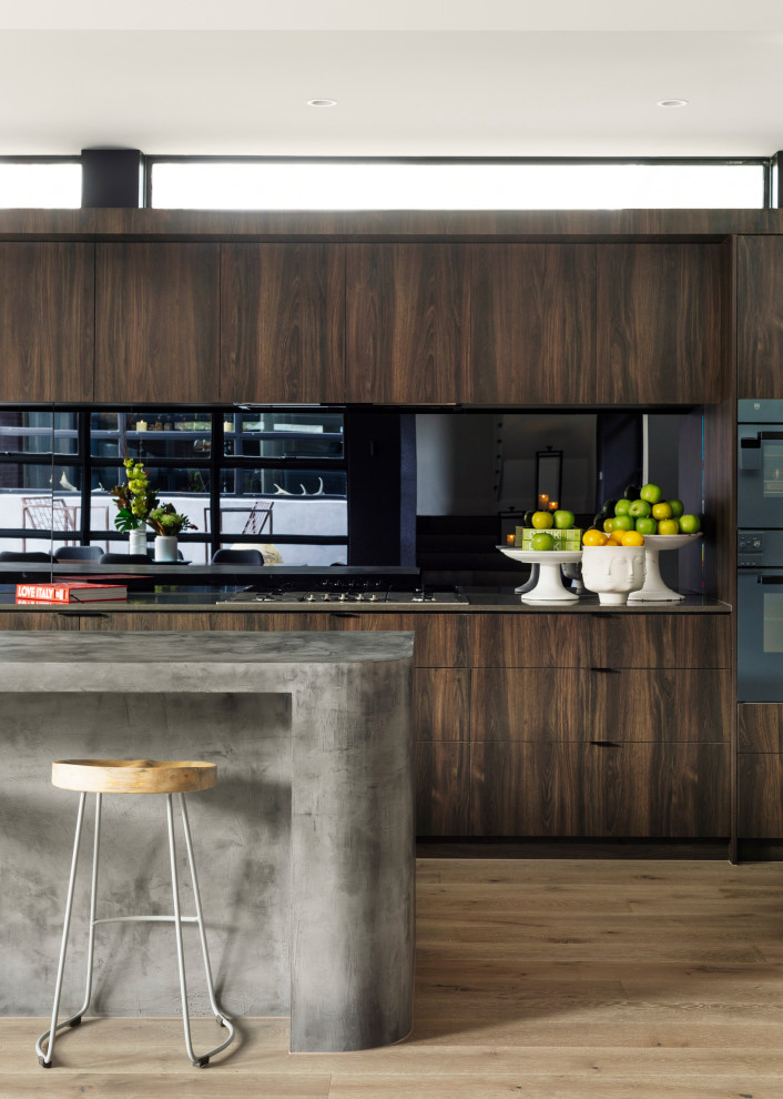 Photo of an expansive contemporary open plan kitchen in Melbourne with dark wood cabinets, concrete benchtops, black splashback, glass sheet splashback, light hardwood floors, with island, grey benchtop, flat-panel cabinets and beige floor.