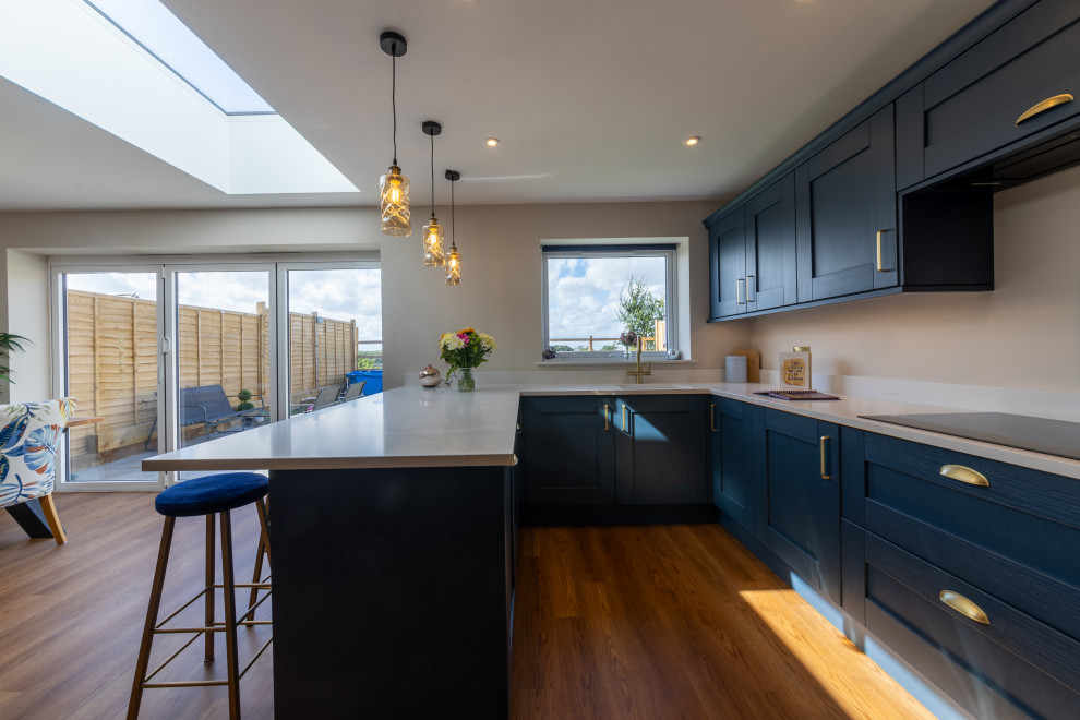 Design ideas for a medium sized modern u-shaped open plan kitchen with a submerged sink, shaker cabinets, blue cabinets, white splashback, marble splashback, black appliances, vinyl flooring, a breakfast bar, white worktops and feature lighting.