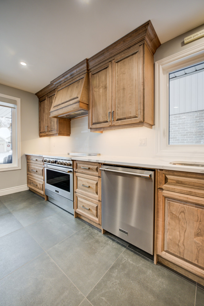 Example of a mid-sized transitional l-shaped gray floor eat-in kitchen design in Toronto with an undermount sink, raised-panel cabinets, medium tone wood cabinets, quartz countertops, white backsplash, ceramic backsplash, stainless steel appliances, an island and white countertops
