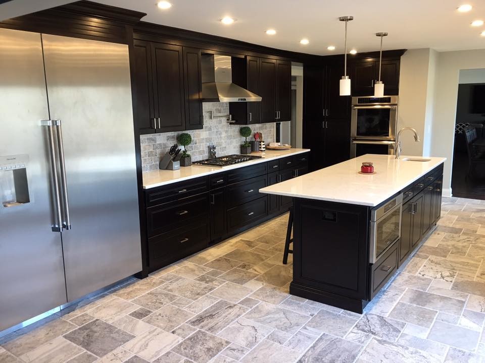 Inspiration for a large transitional l-shaped porcelain tile and beige floor kitchen remodel in Chicago with black cabinets, solid surface countertops, an undermount sink, beaded inset cabinets, gray backsplash, stone tile backsplash, stainless steel appliances and an island