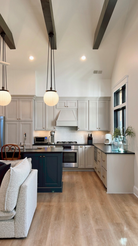 Design ideas for an expansive traditional open plan kitchen in DC Metro with a belfast sink, beige cabinets, soapstone worktops, white splashback, porcelain splashback, stainless steel appliances, laminate floors, an island, brown floors and exposed beams.