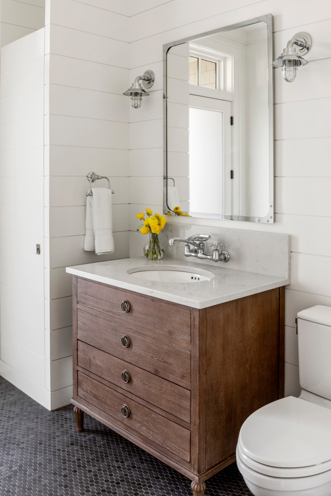 This is an example of a mid-sized country powder room in Boston with white walls, quartzite benchtops, grey benchtops, furniture-like cabinets, medium wood cabinets, a two-piece toilet, mosaic tile floors, an undermount sink, black floor and planked wall panelling.