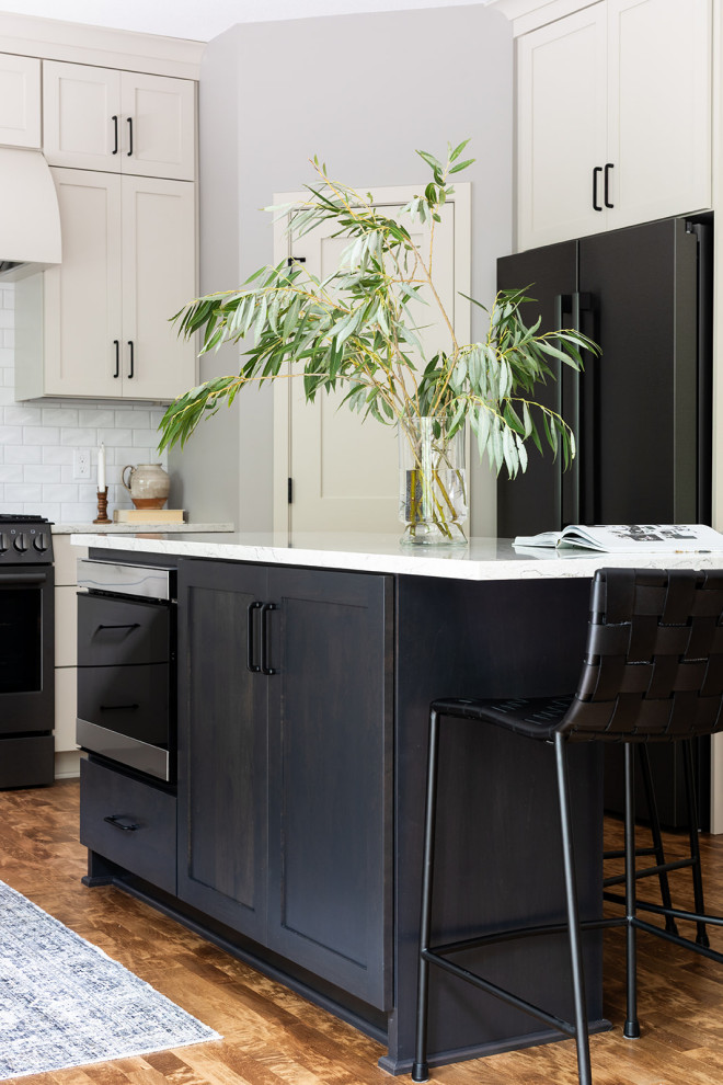 Inspiration for a mid-sized transitional u-shaped medium tone wood floor and brown floor eat-in kitchen remodel with an undermount sink, shaker cabinets, white cabinets, quartz countertops, white backsplash, subway tile backsplash, black appliances, an island and white countertops
