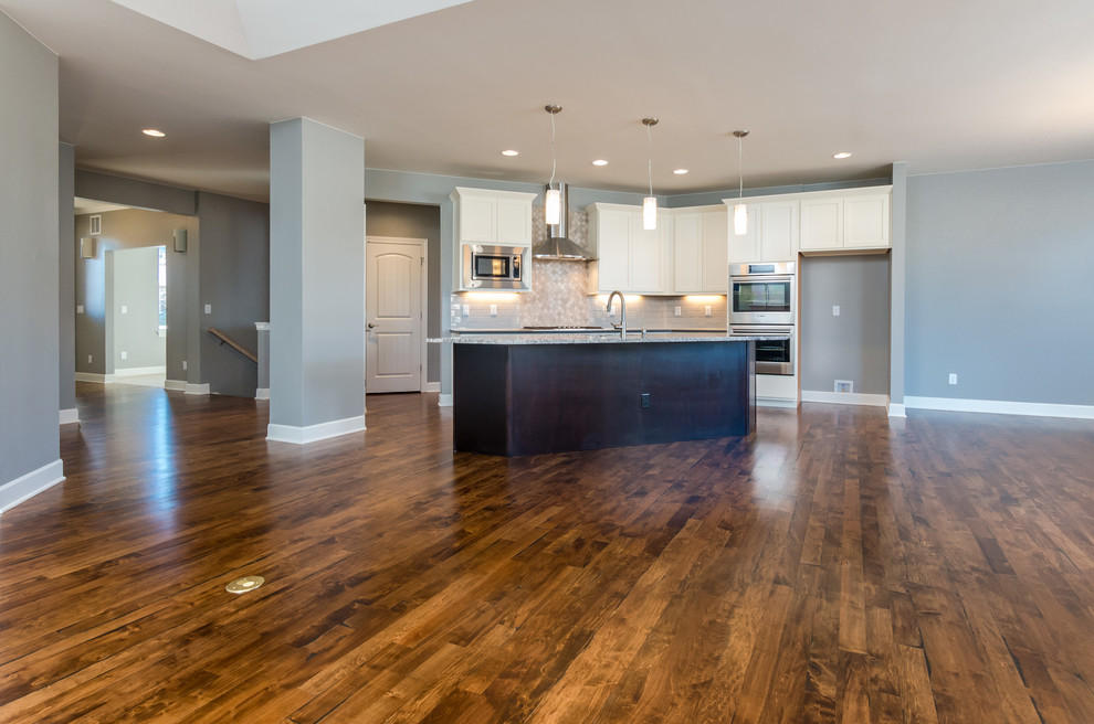 Open concept kitchen - transitional l-shaped medium tone wood floor open concept kitchen idea in Denver with an undermount sink, recessed-panel cabinets, dark wood cabinets, granite countertops, beige backsplash, stone tile backsplash, stainless steel appliances and an island