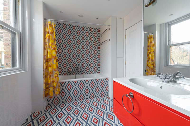 Inspiration for a large contemporary kids bathroom in London with glass-front cabinets, red cabinets, a drop-in tub, a shower/bathtub combo, a wall-mount toilet, white tile, mosaic tile, white walls, mosaic tile floors, an integrated sink, quartzite benchtops, red floor, a shower curtain, white benchtops, a double vanity and a floating vanity.