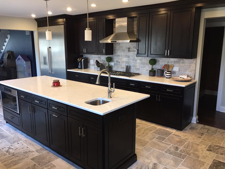 Inspiration for a large transitional l-shaped porcelain tile and beige floor kitchen remodel in Chicago with an undermount sink, beaded inset cabinets, black cabinets, solid surface countertops, gray backsplash, stone tile backsplash, stainless steel appliances and an island