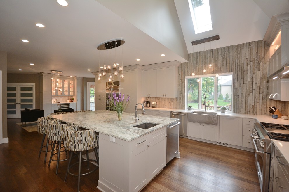 Example of a large transitional u-shaped dark wood floor and brown floor eat-in kitchen design with a farmhouse sink, recessed-panel cabinets, white cabinets, limestone countertops, beige backsplash, porcelain backsplash, stainless steel appliances, an island and gray countertops