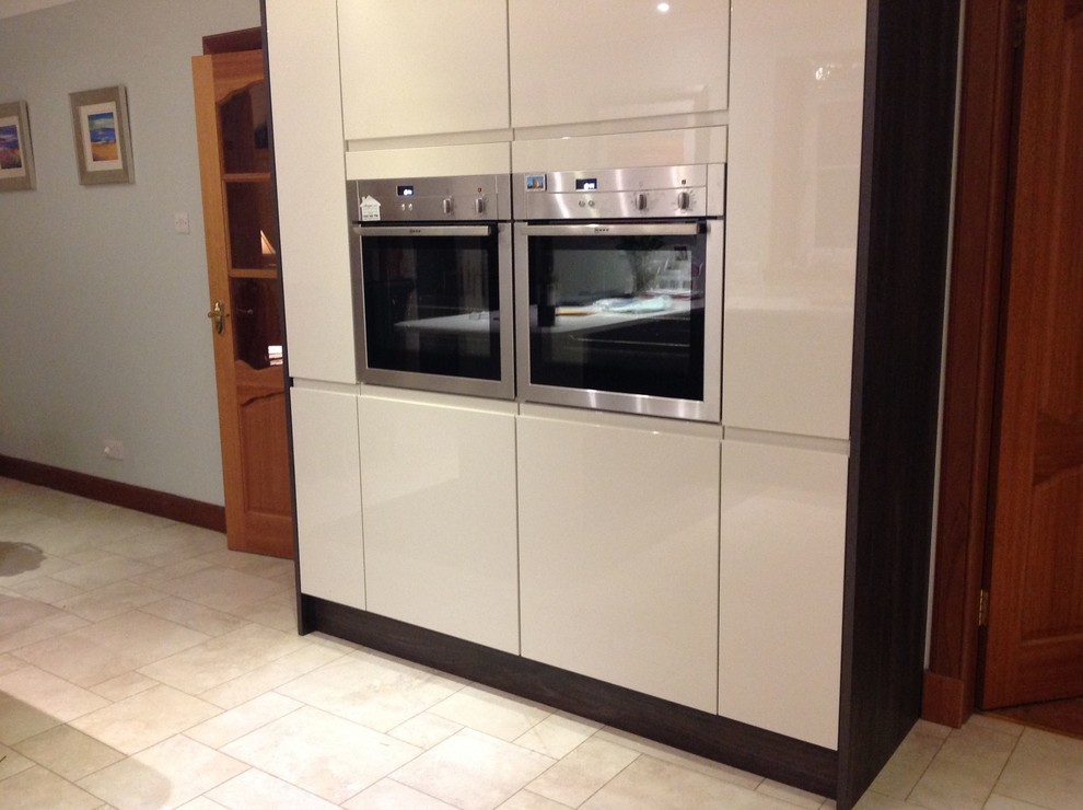 This is an example of a medium sized contemporary l-shaped kitchen/diner with flat-panel cabinets, white cabinets, composite countertops, black splashback, glass sheet splashback, stainless steel appliances and a breakfast bar.