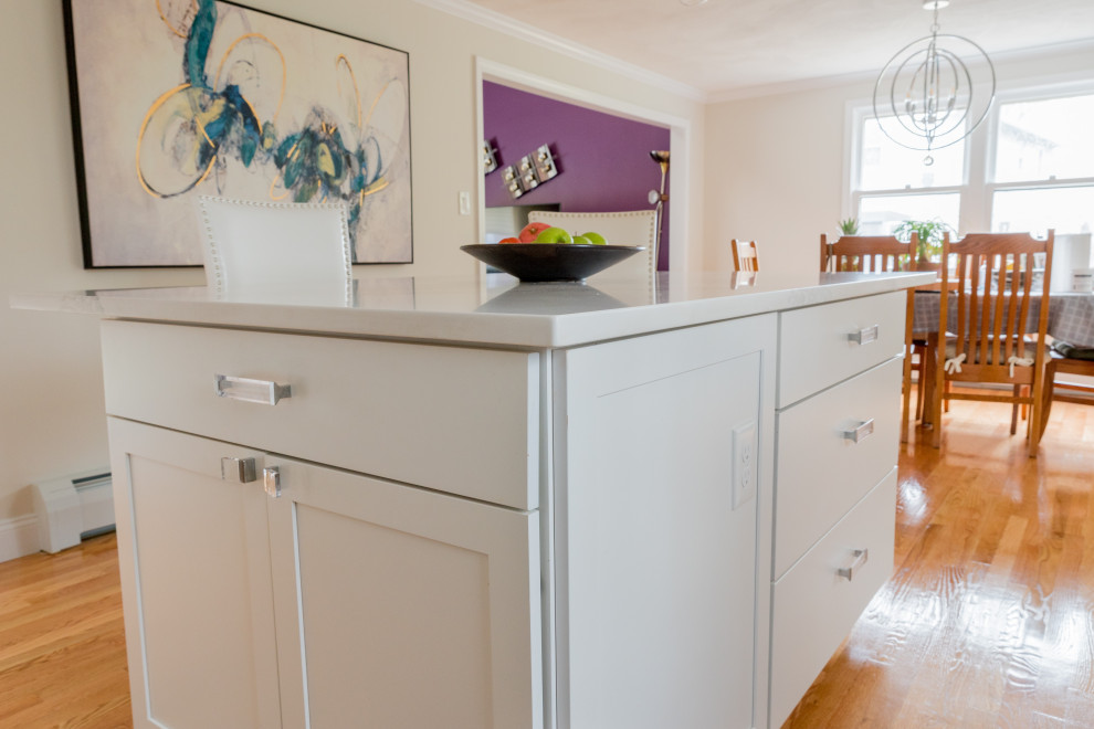 Example of a mid-sized transitional l-shaped light wood floor and brown floor eat-in kitchen design in Boston with a farmhouse sink, shaker cabinets, white cabinets, quartz countertops, gray backsplash, ceramic backsplash, stainless steel appliances, an island and white countertops