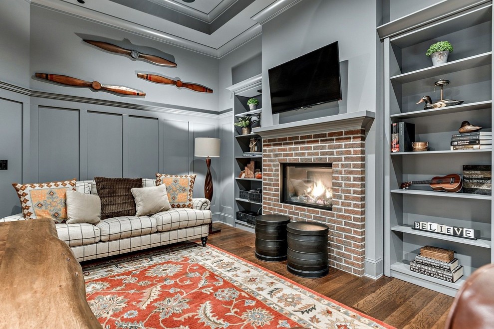 Photo of a mid-sized traditional study room in New York with grey walls, medium hardwood floors, a standard fireplace, a brick fireplace surround, a built-in desk and brown floor.