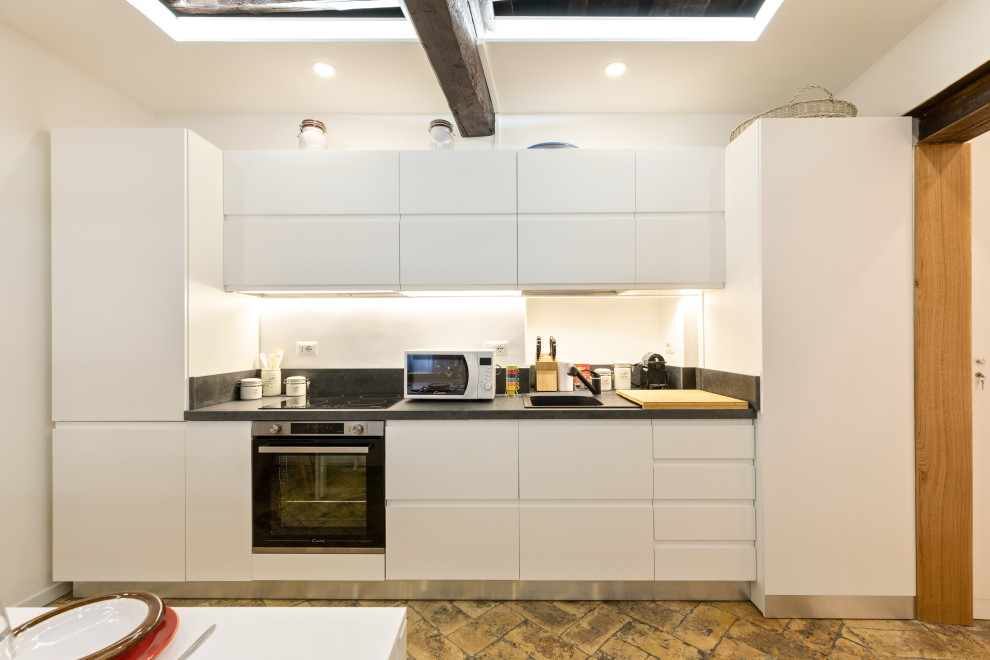 Photo of a small contemporary single-wall eat-in kitchen in Rome with a single-bowl sink, beaded inset cabinets, white cabinets, granite benchtops, grey splashback, granite splashback, black appliances, terra-cotta floors, no island, beige floor and grey benchtop.