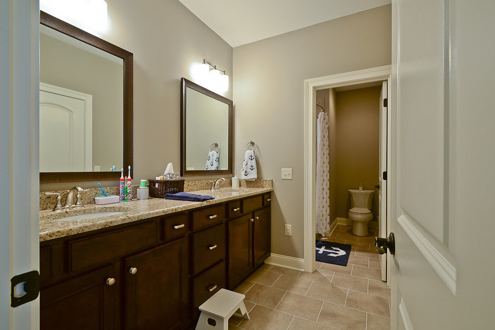 Inspiration for a mid-sized transitional kids bathroom in Indianapolis with an undermount sink, recessed-panel cabinets, dark wood cabinets, granite benchtops, an alcove tub, a shower/bathtub combo, a two-piece toilet, beige tile, porcelain tile, grey walls and porcelain floors.
