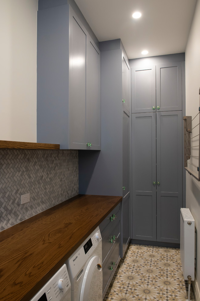 This is an example of a large mediterranean single-wall dedicated laundry room in Melbourne with a drop-in sink, shaker cabinets, grey cabinets, wood benchtops, white walls, ceramic floors, a side-by-side washer and dryer and yellow floor.