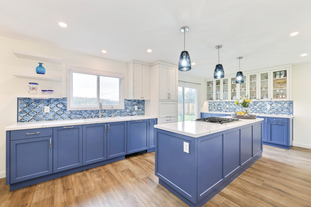 Inspiration for a large classic open plan kitchen in San Francisco with a double-bowl sink, shaker cabinets, blue cabinets, engineered stone countertops, blue splashback, glass tiled splashback, stainless steel appliances, medium hardwood flooring, an island, brown floors and white worktops.