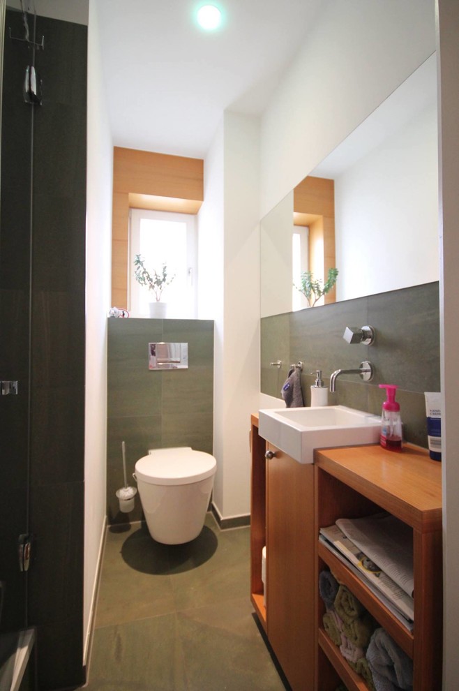 Small contemporary powder room in Stuttgart with flat-panel cabinets, medium wood cabinets, a wall-mount toilet, green tile, cement tile, white walls, cement tiles, an integrated sink and green floor.