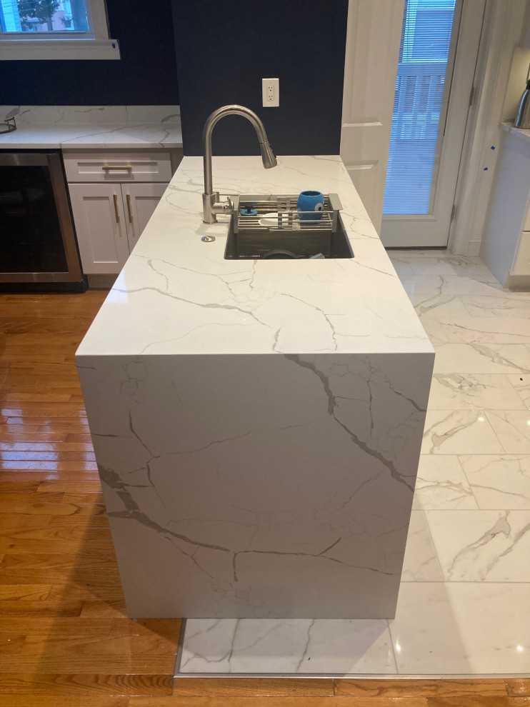 Design ideas for a mid-sized modern galley kitchen in DC Metro with an undermount sink, shaker cabinets, white cabinets, quartzite benchtops, white splashback, stone slab splashback, stainless steel appliances, porcelain floors, with island, white floor and white benchtop.